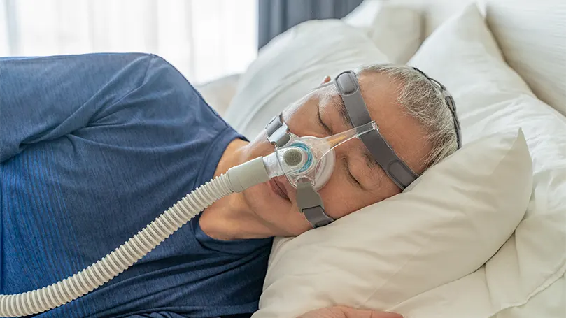 En äldre man sover med CPAP-mask