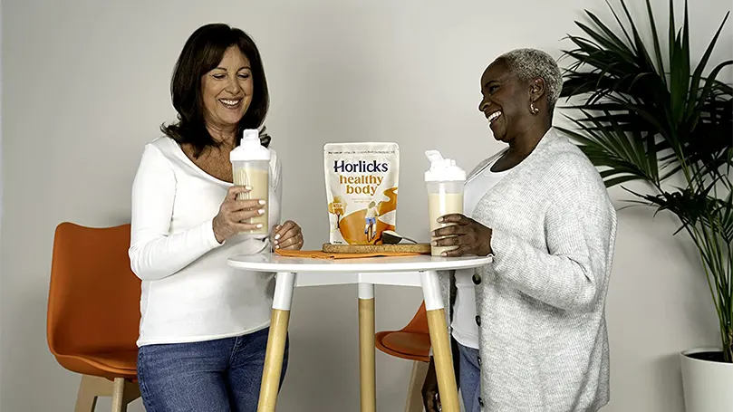 Två kvinnor håller i glas med horlicks och står bredvid ett bord