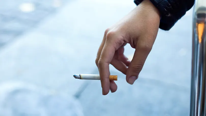 En bild av en persons hand som håller i en cigarett.